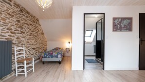 A bedroom with a bed, a chair, a stone wall, a wooden ceiling, a map on the wall, and a doorway leading to another room.