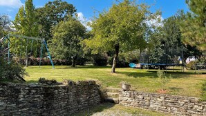 A stone wall, a swing set, and a grassy area with trees.