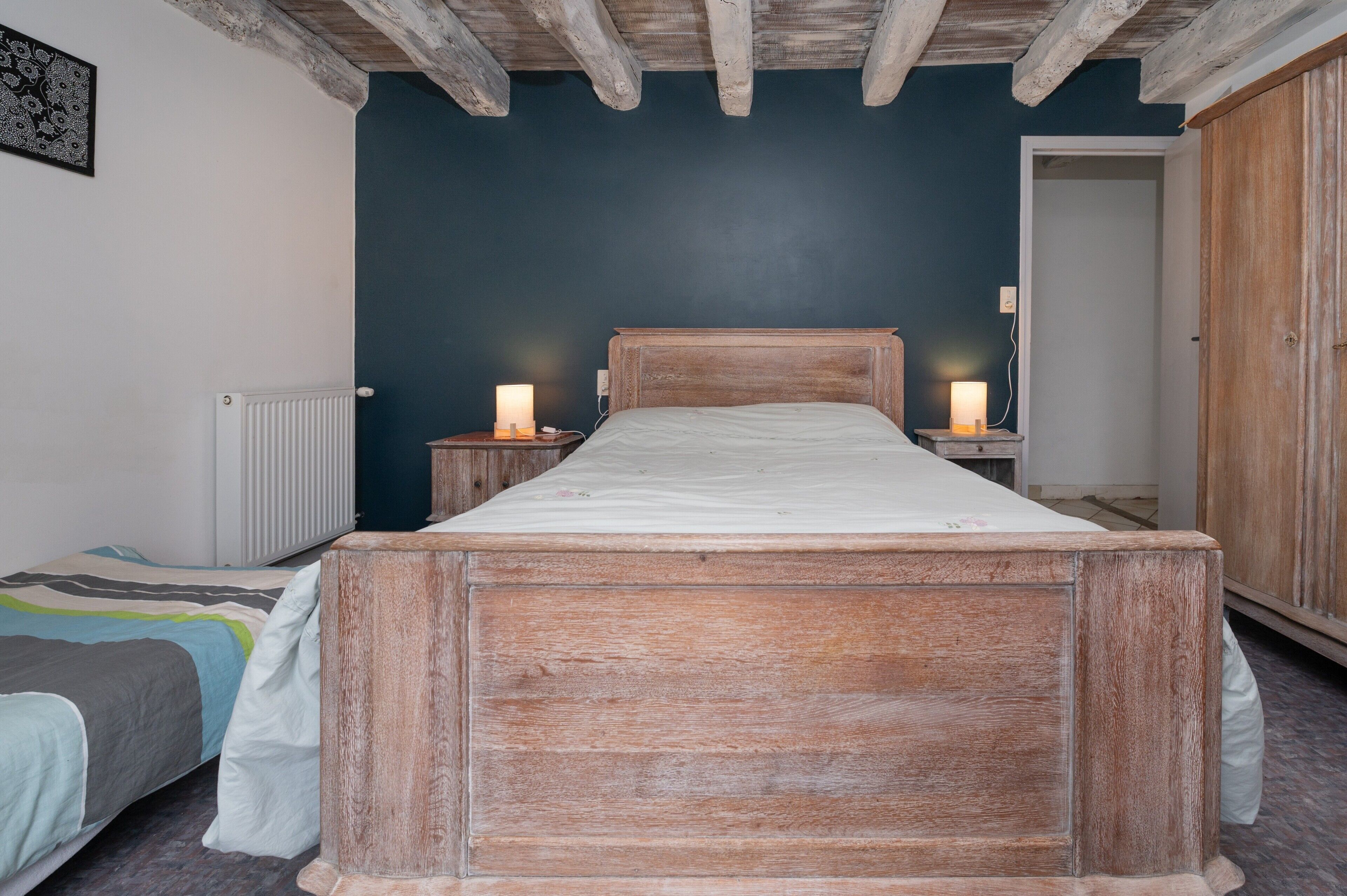 A bedroom with a wooden bed, bedside lamps, a radiator, and a door.