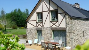 A traditional half-timbered house with a stone facade, a stone chimney, and a patio with outdoor furniture.