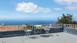 A terrace with a table and chairs, overlooking a coastal cityscape. - Casa Pereira 2: Perfect for Relaxing and Enjoying Beautiful Sunsets (Ponta do Pargo)