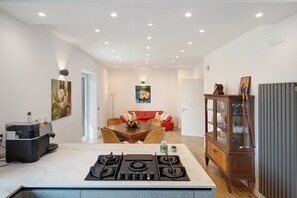 Una cocina moderna con estufa a gas, cafetera y comedor con sofá rojo y mesa.