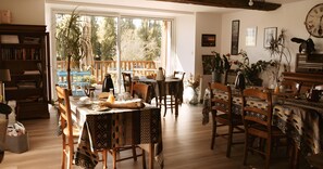 Un comedor con una mesa dispuesta para cuatro, rodeada de sillas de madera, una estantería y vistas al exterior.