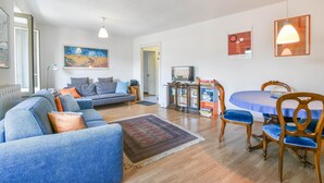 Een woonkamer met een bank, een eettafel met stoelen, een televisie en kunstwerken aan de muren.