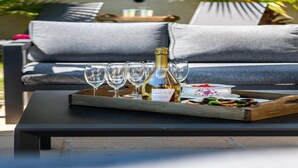 A tray with a bottle of champagne, glasses, and a small dish of food on a table in a sunlit outdoor seating area. - Villa with swimming pool, sauna, fitness, sea view (Biot)