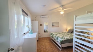 Ein Schlafzimmer mit Etagenbett, Deckenventilator, Klimaanlage, Fenster mit durchscheinenden Vorhängen und Nachttisch mit Vase.