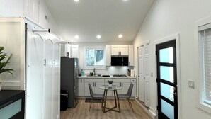 A modern kitchen with white cabinets, a central island, and a black-framed door.