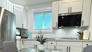 A modern kitchen with white cabinets, a stainless steel refrigerator, a black microwave, and a glass table with two grey chairs.
