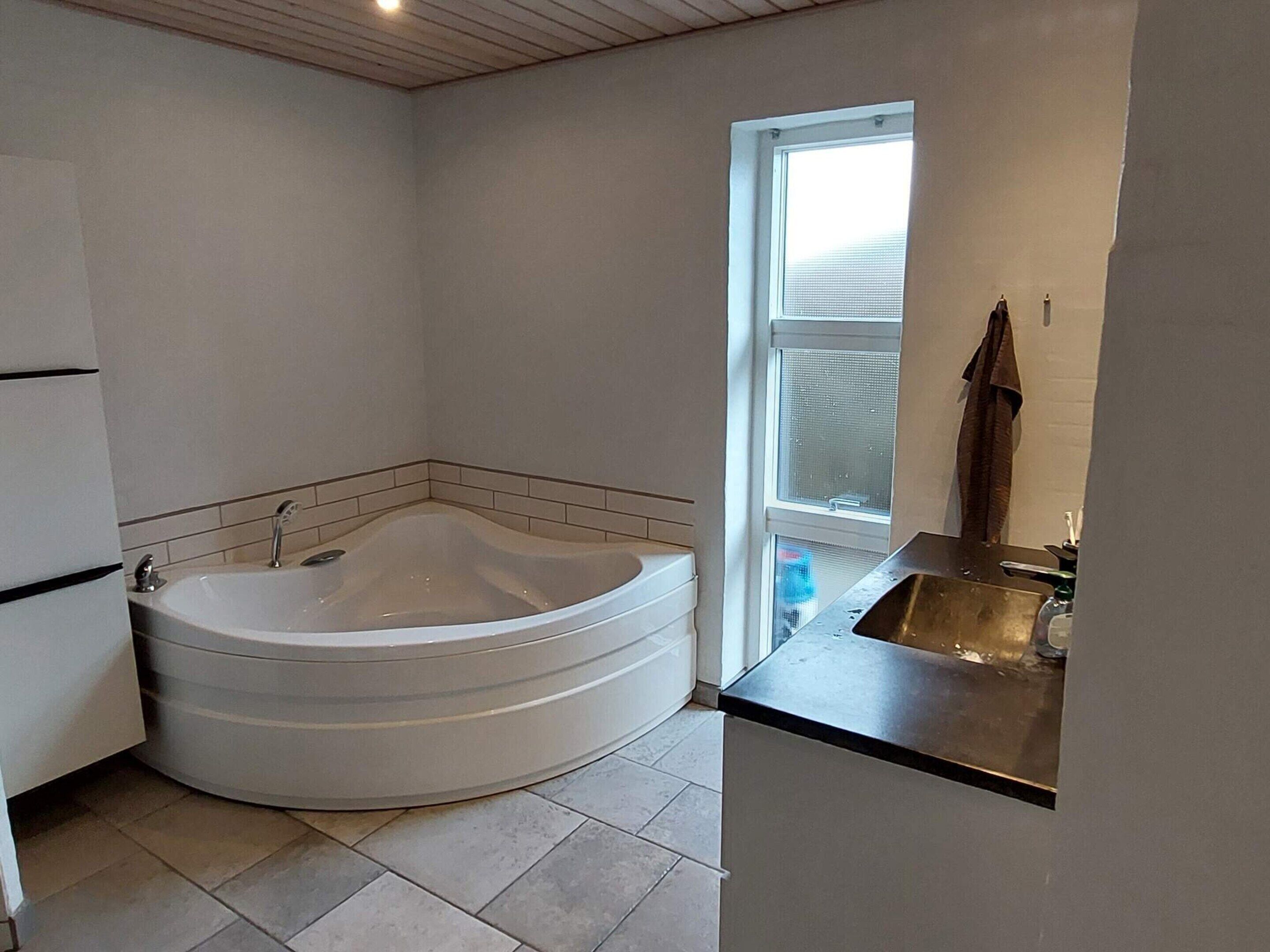 A modern bathroom with a freestanding bathtub, a small sink, and a window providing natural light.