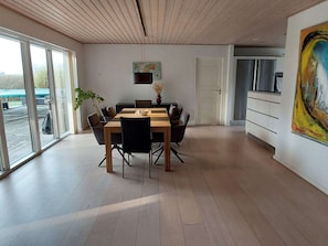 A modern dining area with a wooden table and chairs, a hanging light fixture, and a large window with a view of the outside.