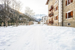 A snow-covered path leading to a building with balconies and a mountainous backdrop.