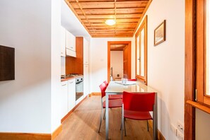 A narrow kitchen with white cabinets, a wooden ceiling, and a dining area with a white table and red chairs.