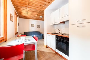 A compact kitchen with white cabinets, a black oven, and a wooden ceiling.