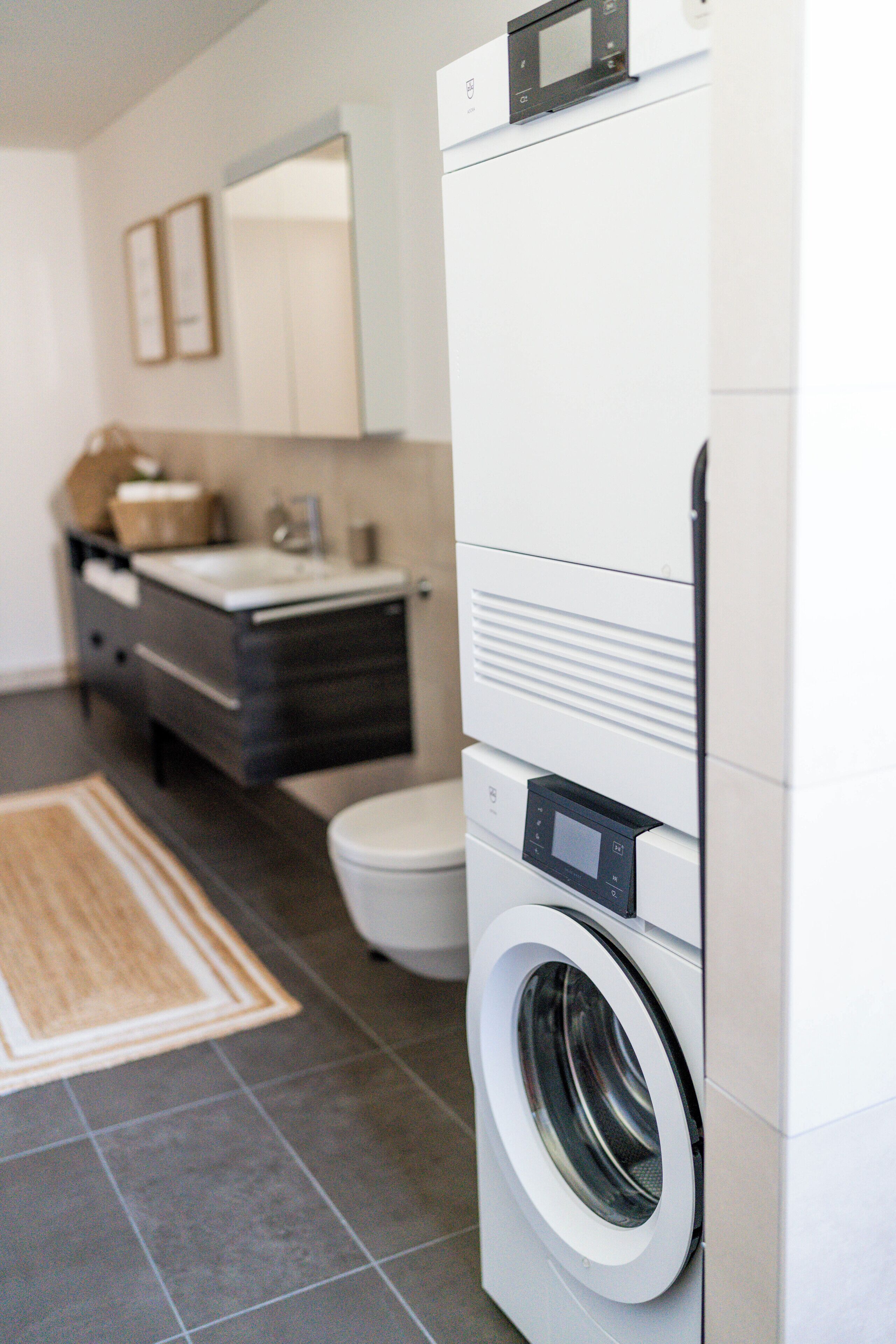 Une salle de bain moderne équipée d’un lave-linge intégré, de toilettes et d’un meuble-lavabo avec un miroir.