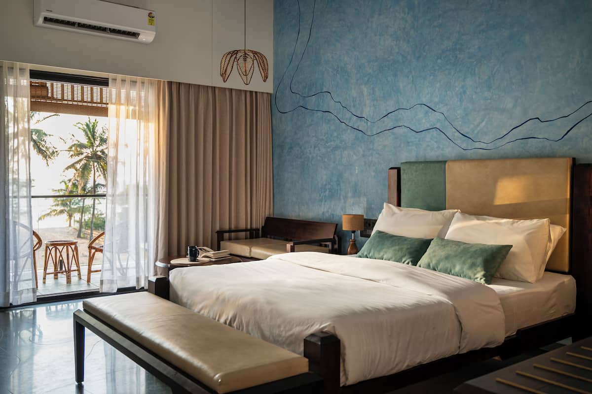 A hotel room with a large bed, a desk, and a view of palm trees through sheer curtains.