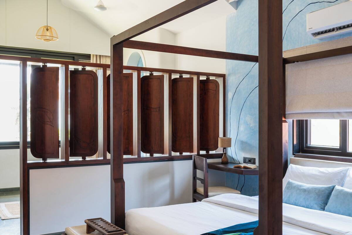 A four-poster bed with a wooden frame, a bedside table, a chair, and a window with curtains.