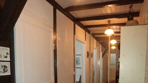 A hallway with wooden flooring, a white door, and a bed with a red blanket. - In the heart of the village, 70 m2 Landes house ideal for a family of 4 people (Léon)