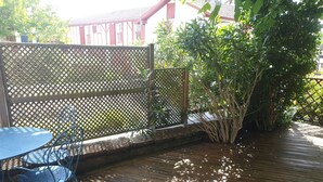 A wooden deck with a table and chairs, surrounded by a lattice fence and greenery. - In the heart of the village, 70 m2 Landes house ideal for a family of 4 people (Léon)