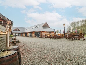 Un bâtiment rustique avec une cour en gravier, des tables et des chaises en bois, et un grand tonneau.
