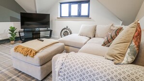 A cozy living room with a sofa, ottoman, and a television on a stand. - The Walnut Room - Windmill Country Retreats (Melton Mowbray)