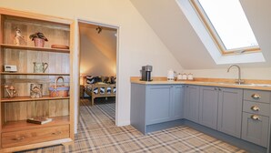 A compact kitchen with a skylight, a wooden shelf unit, and a plaid-patterned floor. - The Walnut Room - Windmill Country Retreats (Melton Mowbray)