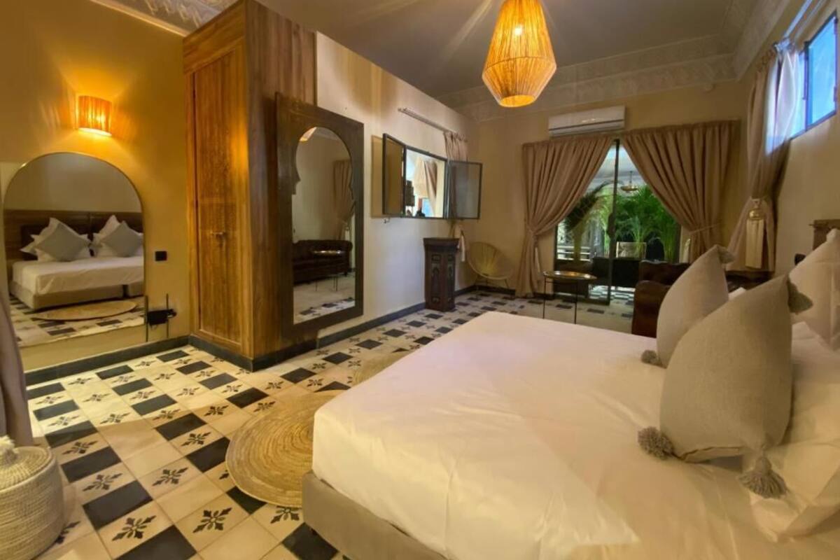 A spacious bedroom with a large bed, a mirror, a wooden wardrobe, and a view of greenery outside.