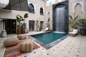 A pool area with a waterfall, potted plants, and outdoor seating. - RIAD DAR COUSCOUS (Marrakech)
