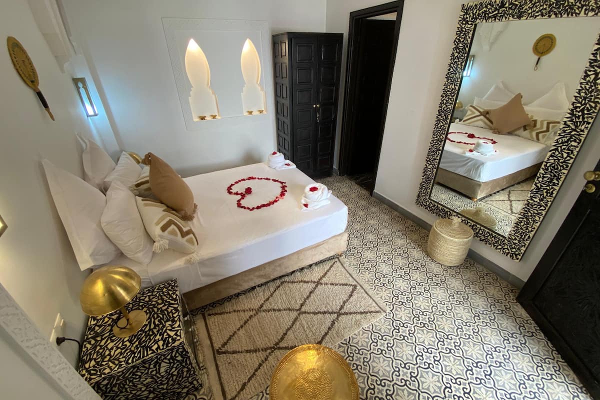 A bedroom with a bed, a mirror, a door, and a patterned floor.