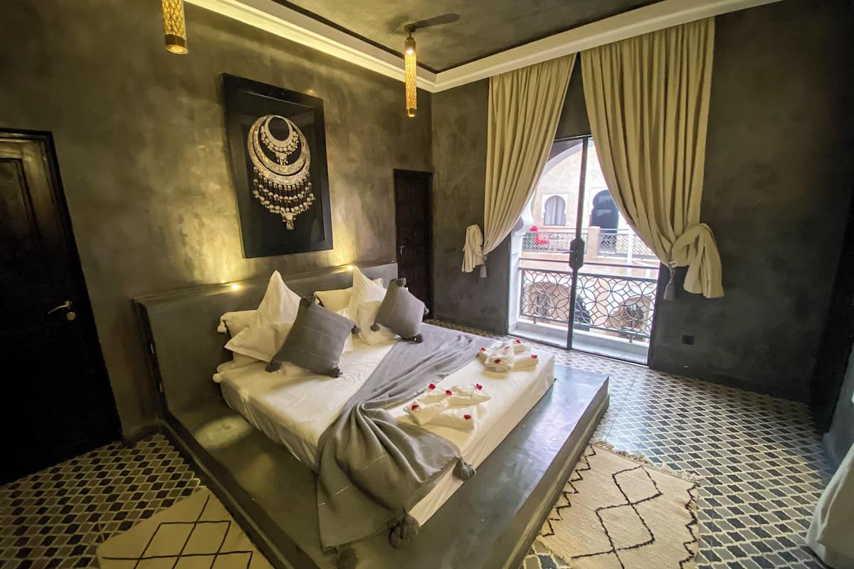 A modern bedroom with a large bed, a decorative wall piece, and a view through a window.