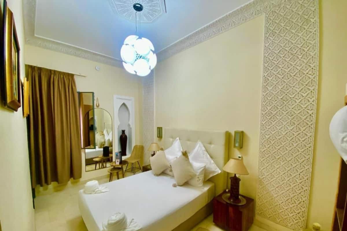 A hotel room with a bed, bedside lamps, a mirror, a small table, and a decorative wall panel.