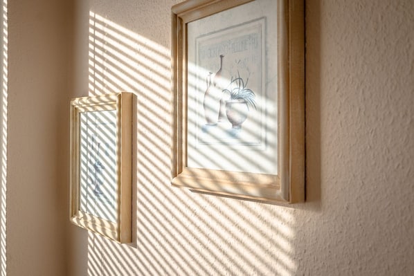 Zwei gerahmte Kunstwerke an einer Wand, wobei das Sonnenlicht Schatten wirft.