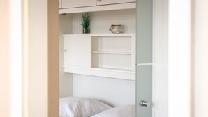 Un dormitorio con cama, paredes blancas y un estante empotrado con una planta y un objeto decorativo.