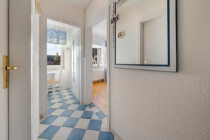 A hallway with a checkered floor, a white door with a golden handle, and a mirror on the wall.