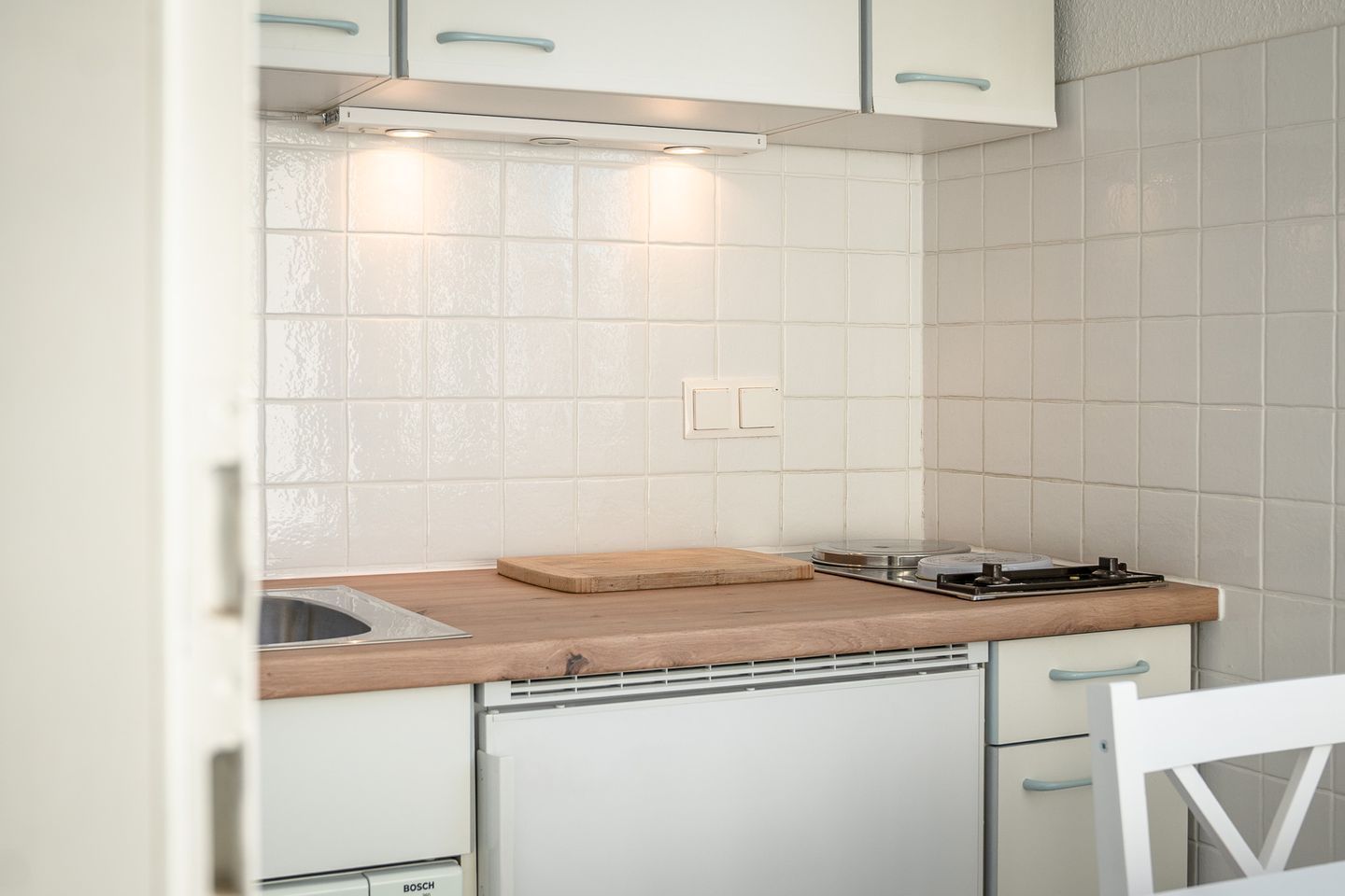 A compact kitchen with white cabinets, a wooden countertop, and a Bosch dishwasher.