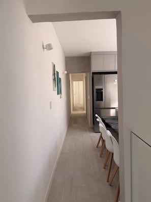 A modern kitchen with a refrigerator, a dining area with chairs, and a hallway leading to another room. - Tons de Cinza (Itatiba)