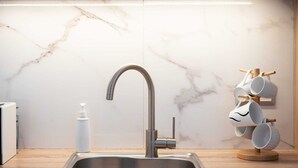 Une cuisine moderne dotée d’un évier en acier inoxydable, d’un pare-feu en marbre et d’un porte-tasses où sont rangées des tasses blanches.