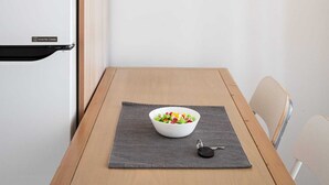 Une cuisine moderne avec un réfrigérateur blanc, une table en bois sur laquelle se trouve un saladier rempli de fruits, et un luminaire suspendu.