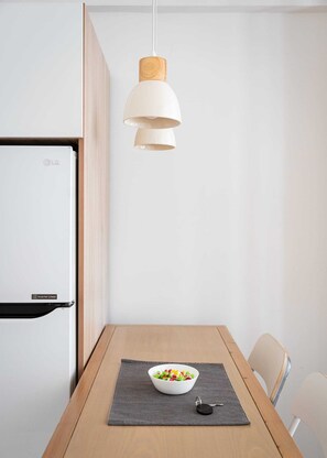 A modern kitchen with a white refrigerator, a wooden table with a bowl of fruit, and a pendant light. - Acropolis Cozy Living, Apartment (Athens)