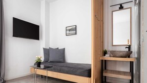 Une chambre moderne comprenant un lit, une télévision, une petite table de chevet et une salle de bain avec un lavabo et un miroir.