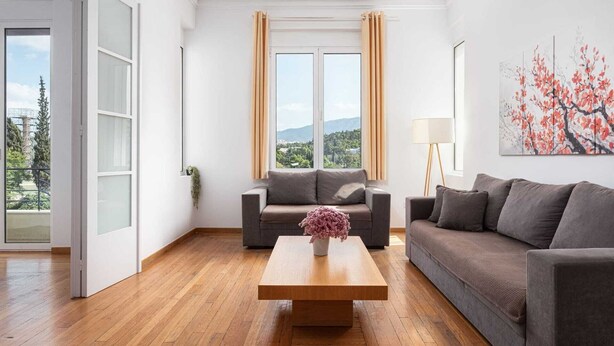 Ein modernes Wohnzimmer mit einer Couch, einem Couchtisch und Blick auf eine gebirgige Landschaft durch große Fenster.