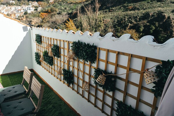 A balcony with a wooden lattice wall, green plants, and a view of a town in the background.