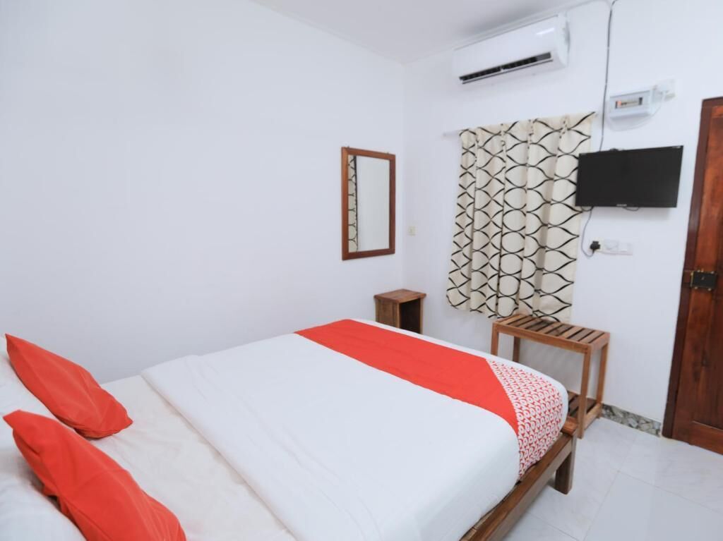 Un dormitorio con cama, una mesita de noche de madera, un televisor montado en la pared y una puerta.