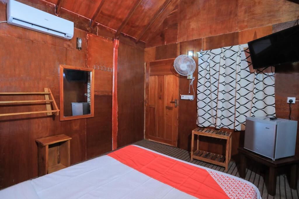 Ein Zimmer mit Holzboden, einem Bett, einem kleinen Tisch, einem Ventilator und einem Fernseher.
