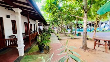 Un espace extérieur abrité, doté d’une rangée de bancs en bois, de plantes en pot et d’un chemin menant à une zone piscine.