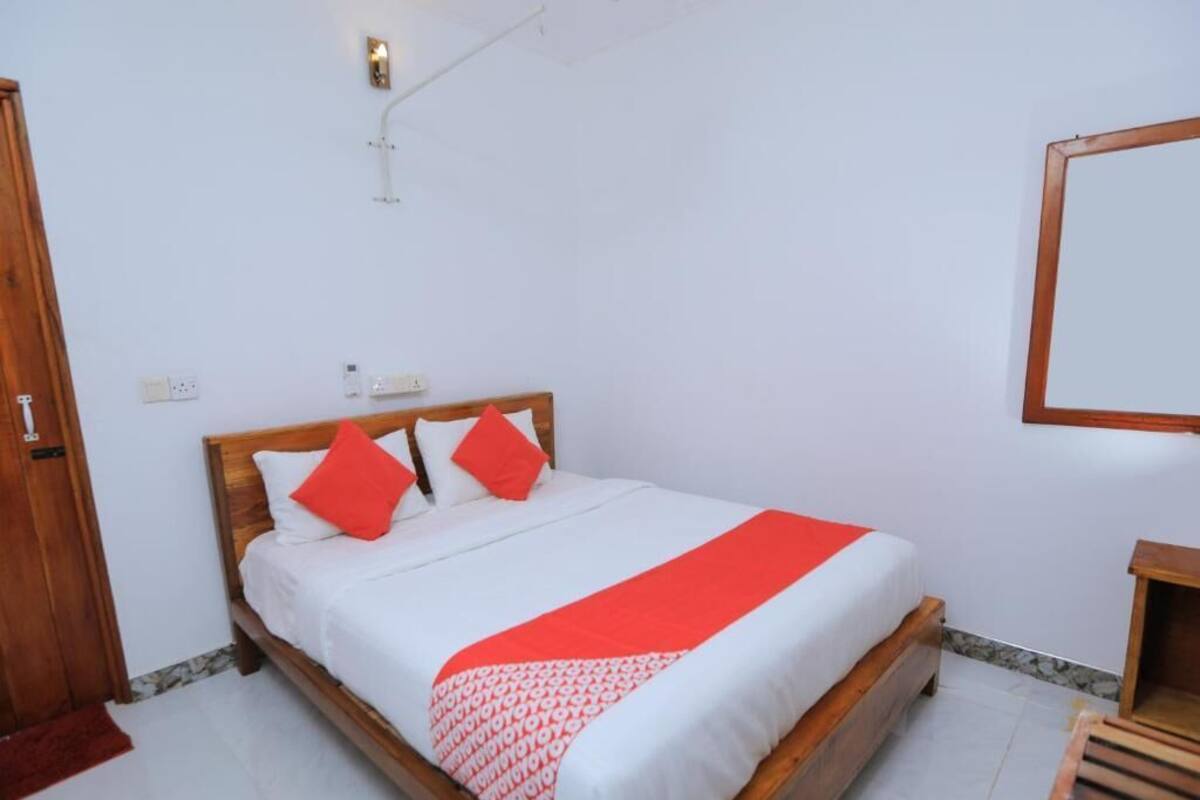 A neatly made bed with a wooden frame, white bedding, and red accents.