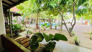 A covered outdoor area with potted plants, a pool, and a building in the background.