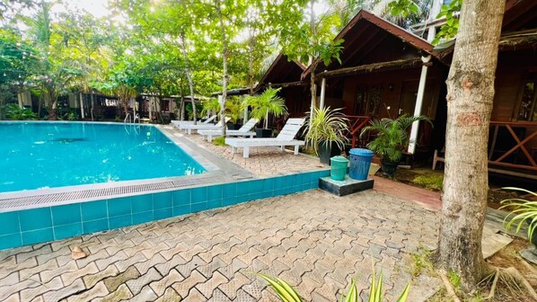 A swimming pool with lounge chairs, a tiled deck, and wooden structures. - Trinco Star Cabana (Trincomalee)