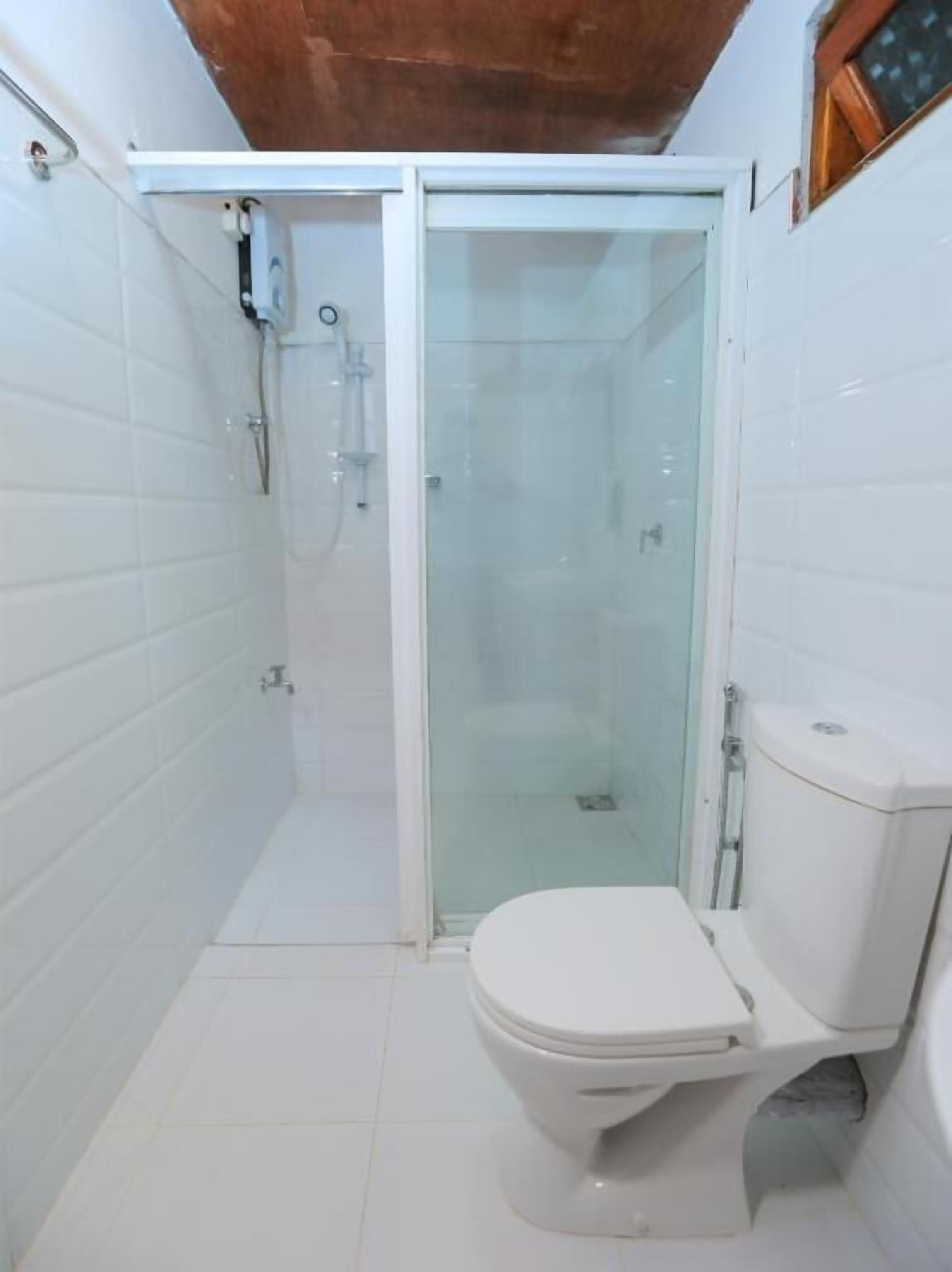 Un bagno piccolo e compatto con piastrelle bianche, una cabina doccia in vetro e un water bianco.