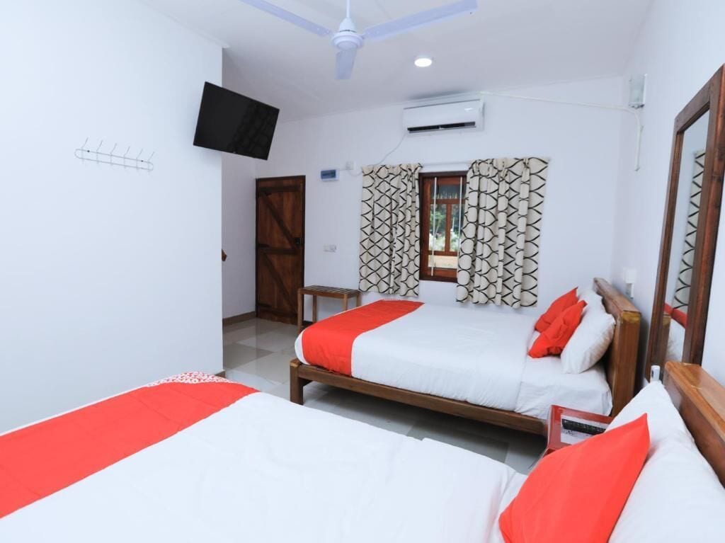 A bedroom with two beds, a ceiling fan, a mounted TV, and a window with patterned curtains.