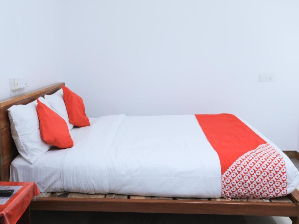 Una cama individual con cabecera de madera, ropa de cama blanca y detalles en rojo.
